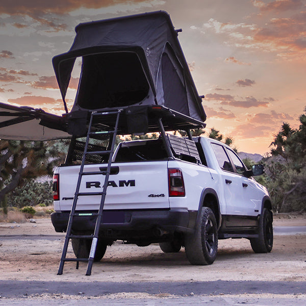 White RAM truck with a rooftop tent in a desert setting during sunset.