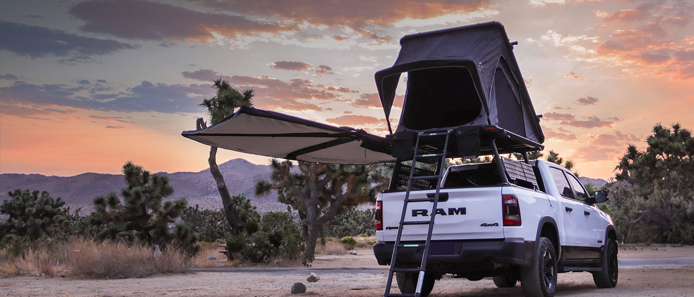 White truck with a rooftop tent parked in a desert landscape at sunset.