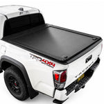 A double t-slot rail retractable cover installed on the bed of a white Toyota Tacoma 4x4 pickup truck, shown from a rear three-quarter angle against a white studio background.