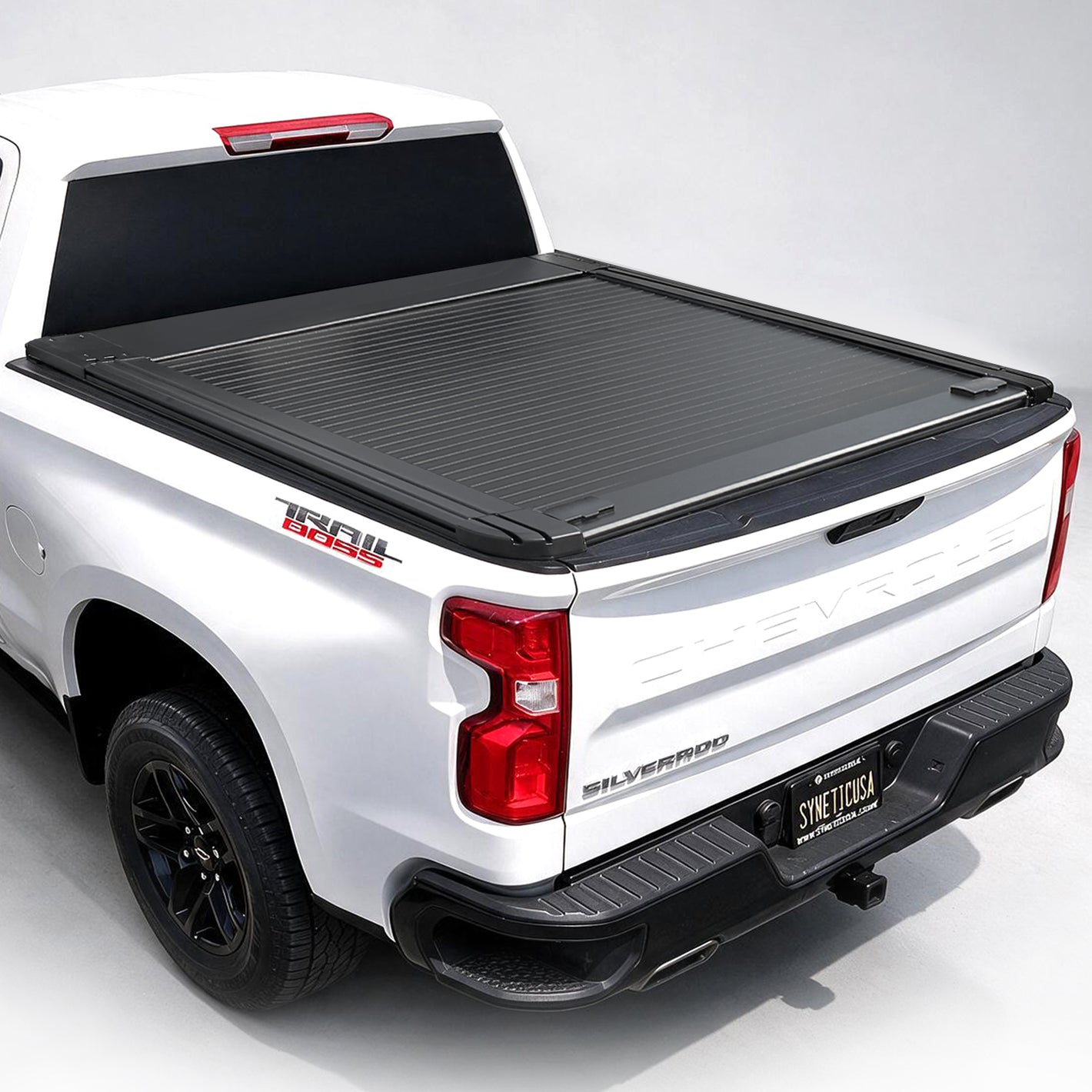 Black roll-up truck bed cover installed on the bed of a white Chevrolet Silverado, shown from a rear three-quarter angle on a white studio background.