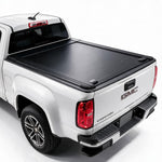 A black roll-up truck bed cover installed on the bed of a white GMC Canyon pickup truck, shown from a rear three-quarter angle on a white studio background.