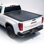 A black roll-up truck bed cover installed on the bed of a white GMC Sierra pickup truck, shown from a rear three-quarter angle on a clean white studio background.