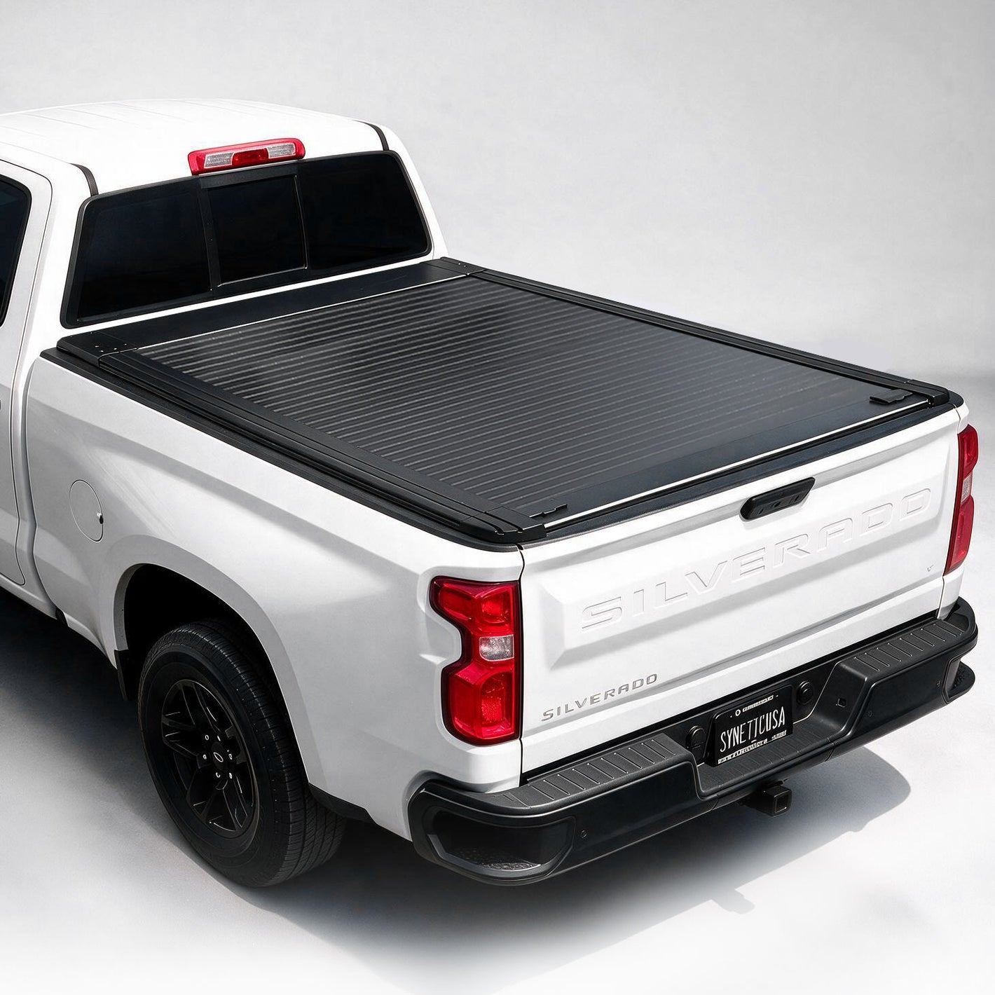 A black ribbed hardtop truck bed cover installed on the bed of a white pickup truck, shown from a rear three-quarter angle against a light gray studio background.