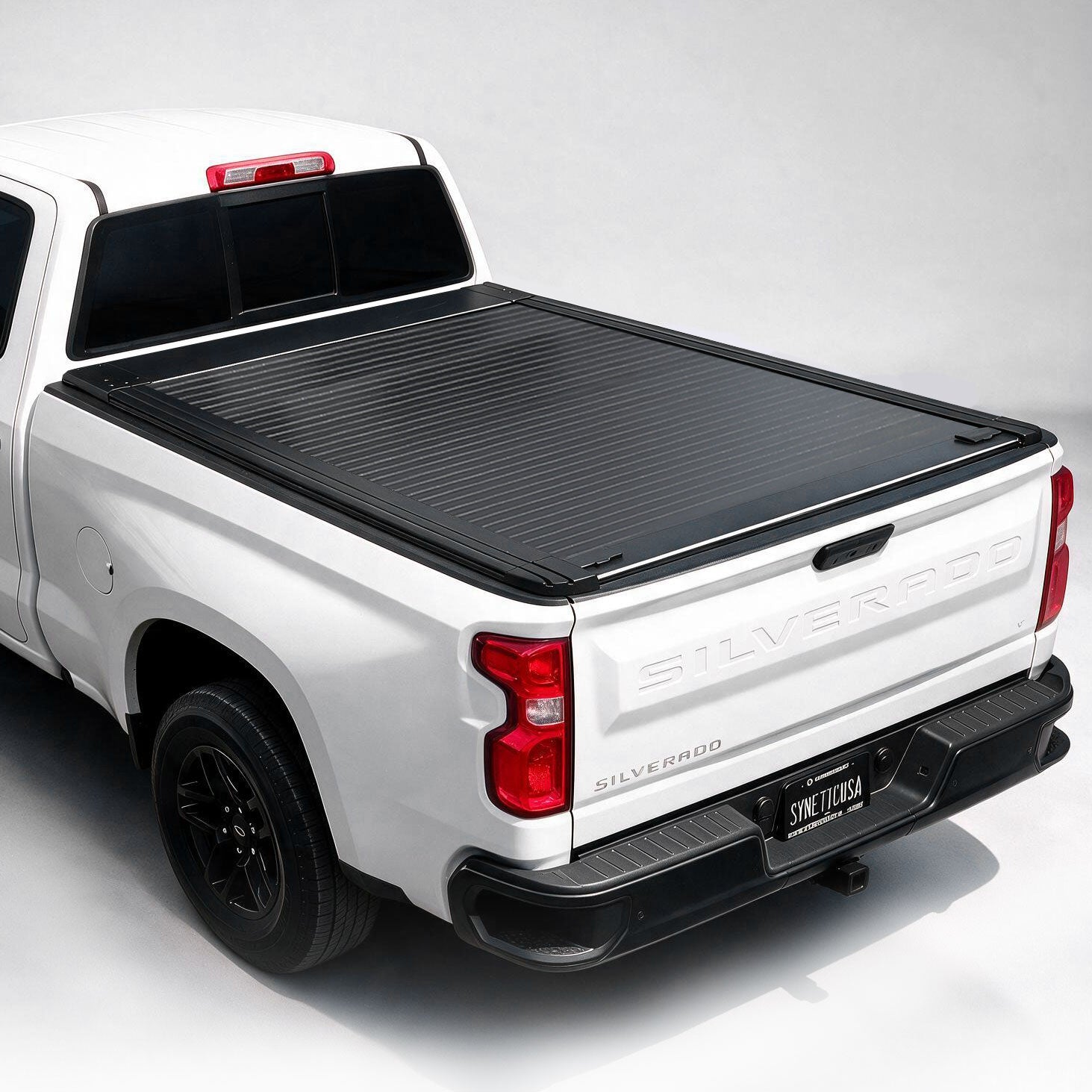 A black ribbed hardtop truck bed cover installed on the bed of a white pickup truck, shown from a rear three-quarter angle against a light gray studio background.