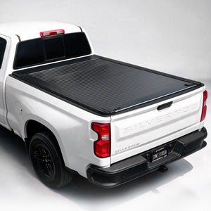 A black ribbed hardtop truck bed cover installed on the bed of a white pickup truck, shown from a rear three-quarter angle against a light gray studio background.