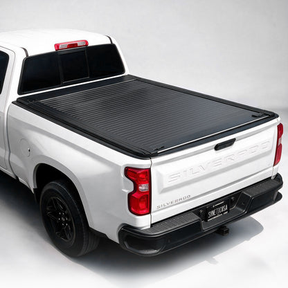 A black ribbed hardtop truck bed cover installed on the bed of a white pickup truck, shown from a rear three-quarter angle against a light gray studio background.