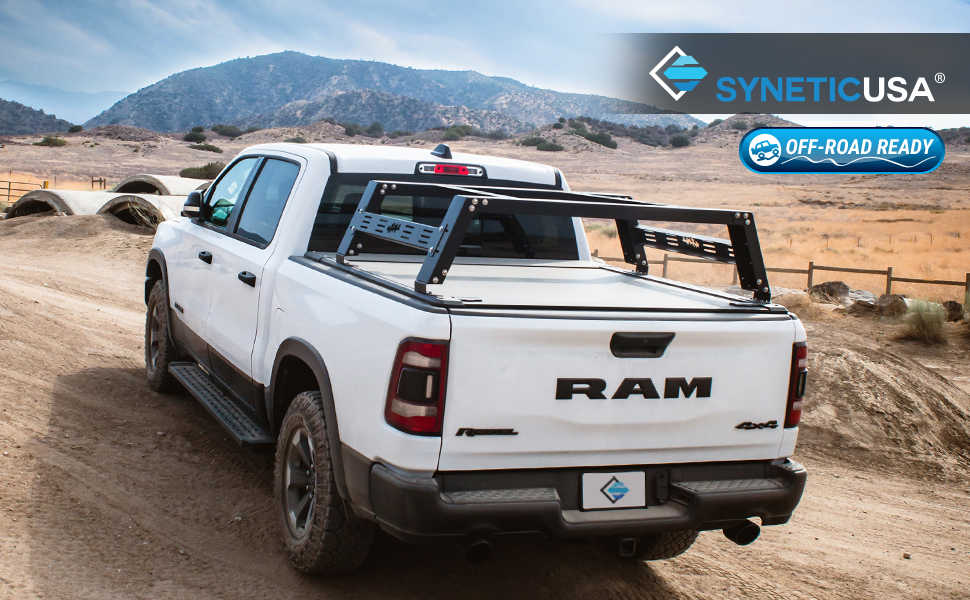 White RAM truck with a bed rack on a dirt road, featuring syneticusa branding.