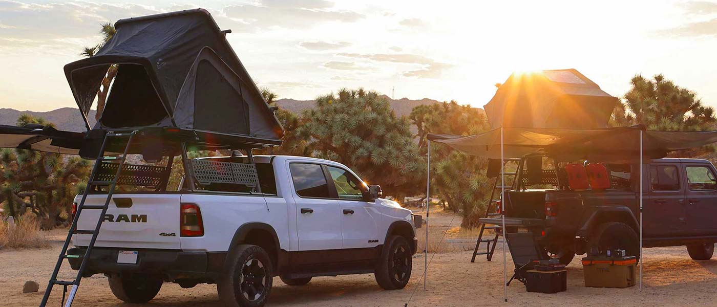 Two trucks with rooftop tents in a desert setting during sunset.