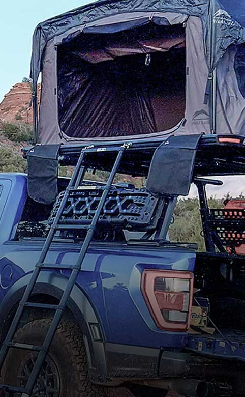 Blue truck with an open rooftop tent in a natural setting