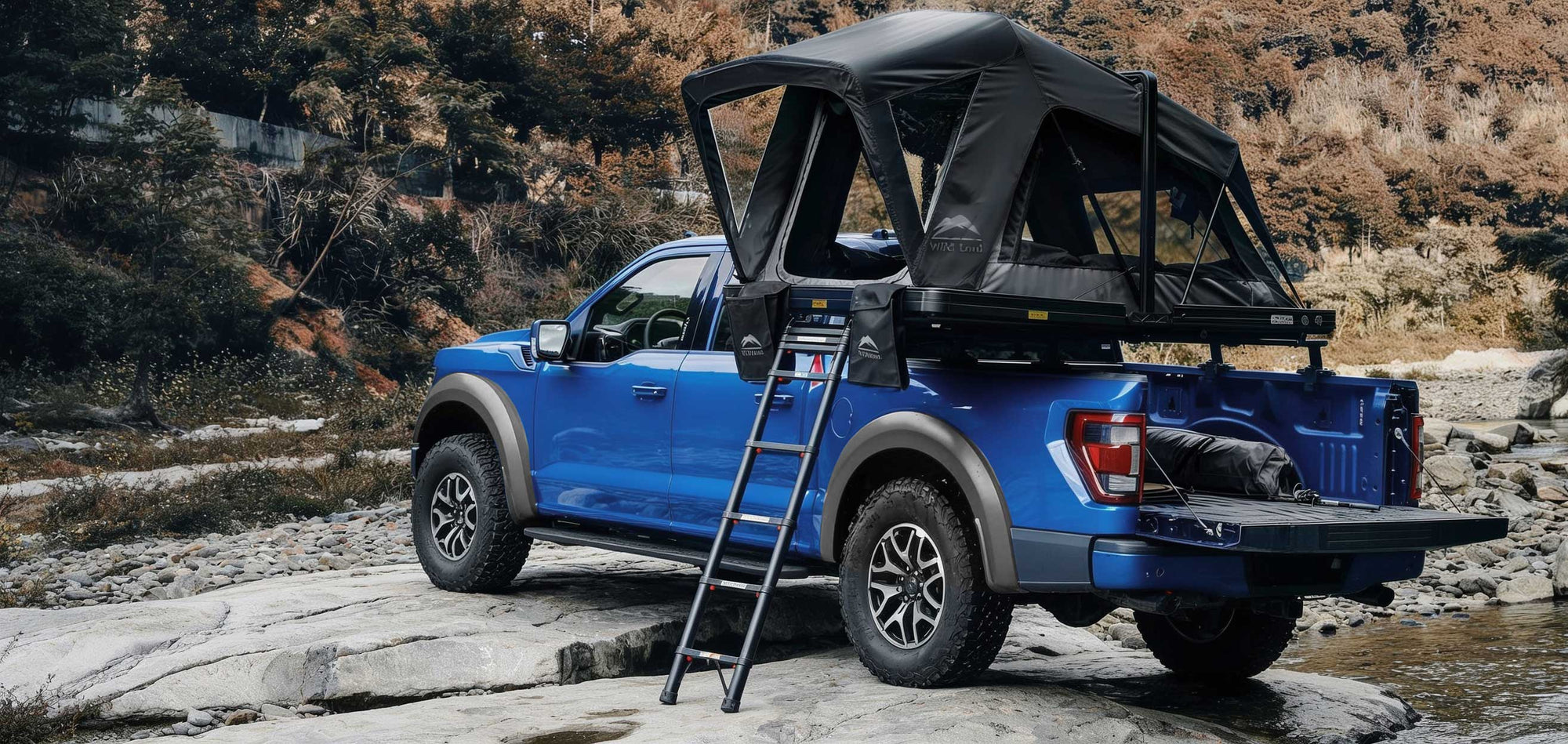 Blue truck with a rooftop tent and ladder on a rocky trail
