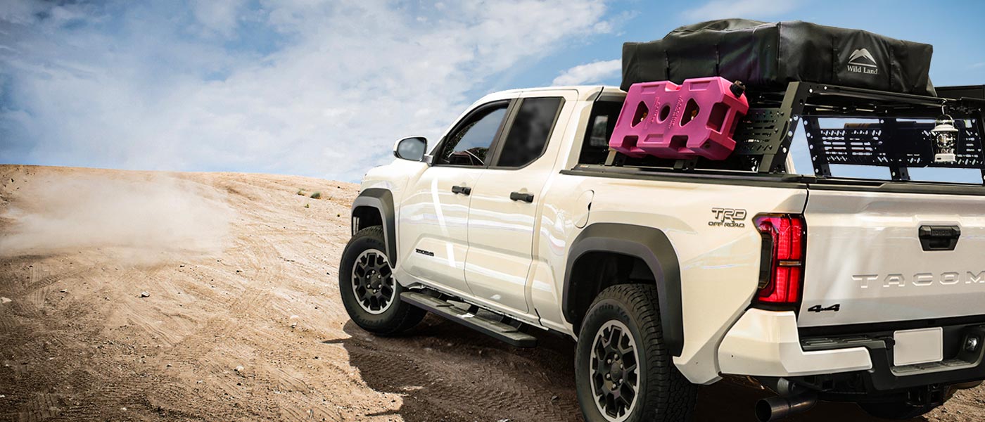 White truck with a roof rack and pink toolbox on a dirt road
