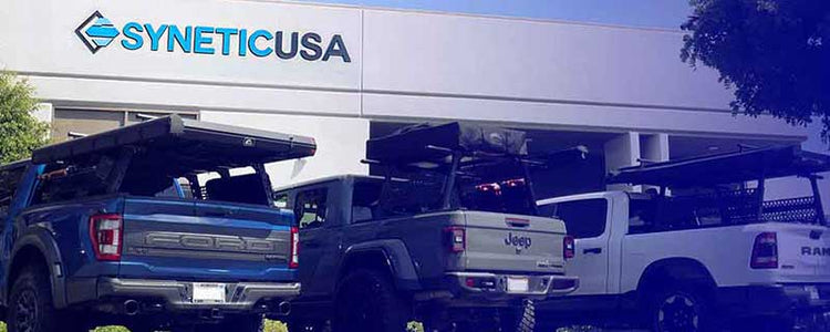 Three trucks parked in front of a building with 'Synetic USA' branding.