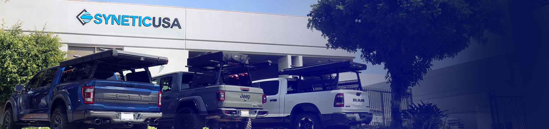 Three trucks parked in front of a building with 'Synetic USA' branding.