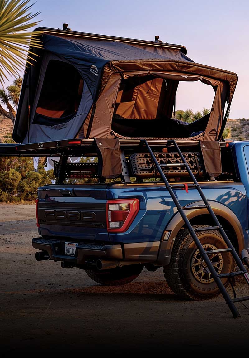 Blue truck with a Dessert cruiser rooftop tent and ladder in a desert setting